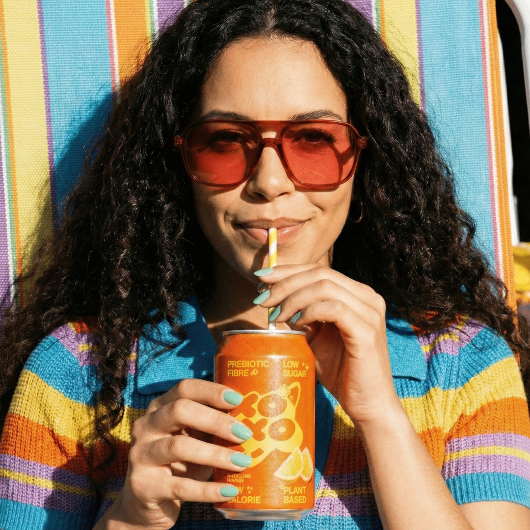 Woman enjoying prebiotic soda benefits while relaxing in a colorful chair, sipping from a can with a straw.