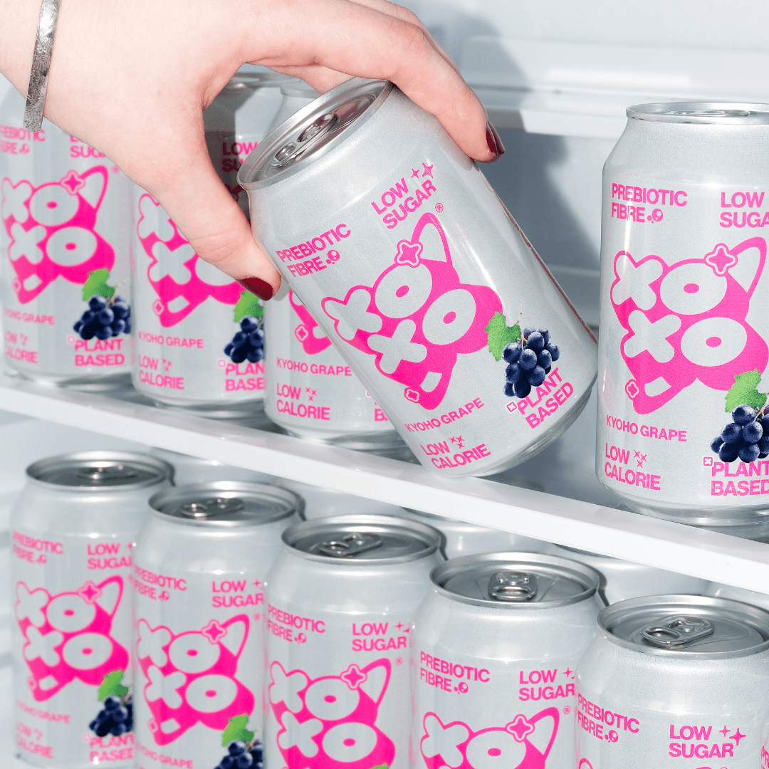 Kyoho Grape Prebiotic Soda | XOXO Limited Edition - 12 Pack cans in a refrigerator with a hand reaching for one.